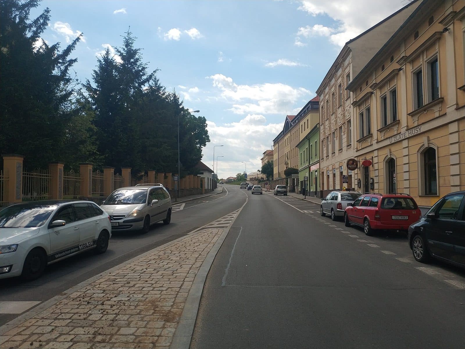 Ulice Čelakovského v Písku, vlevo plot se zděnými sloupky a vzrostlé jehličnany, vpravo řada měšťanských domů a zaparkovaná auta