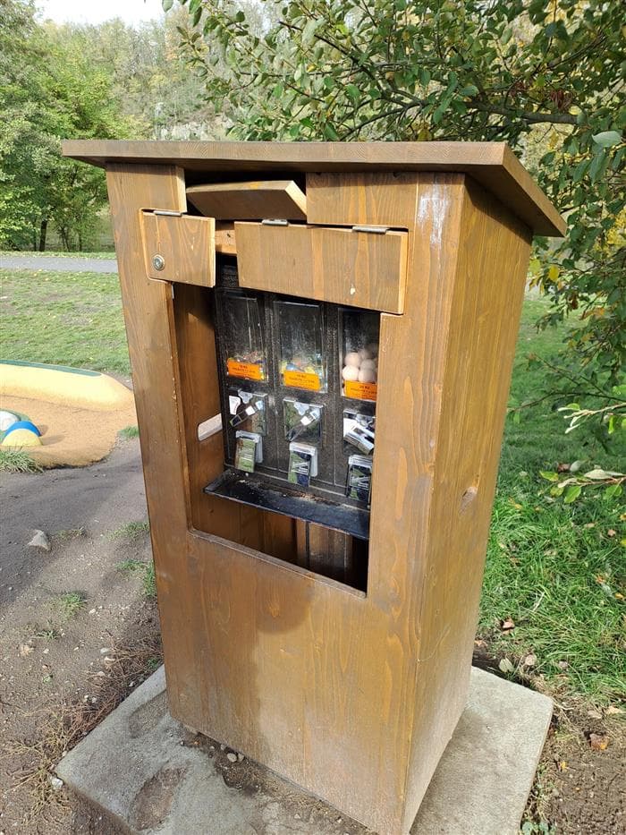 Dřevěná budka s automatem na kuličky u kuličkového hřiště v Písku s poškozenými dvířky nad prodejními šachtami