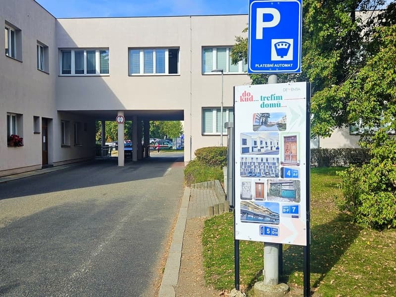 Venkovní panel s nápisem Dokud trefím domů a fotkami dveří a vchodů domů, stojí u vjezdu do areálu Nemocnice Písek pod značkou platebního automatu na parkovné