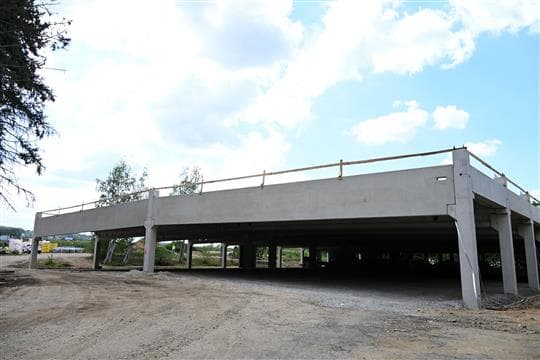 Rozestavěné betonové etážové parkoviště na sídlišti Jih v Písku se střešní deskou na sloupech a štěrkovou plochou před ním