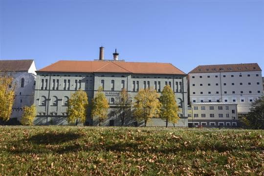 Budova písecké Sladovny s nápisem na fasádě při pohledu od řeky Otavy, před ní podzimní stromy
