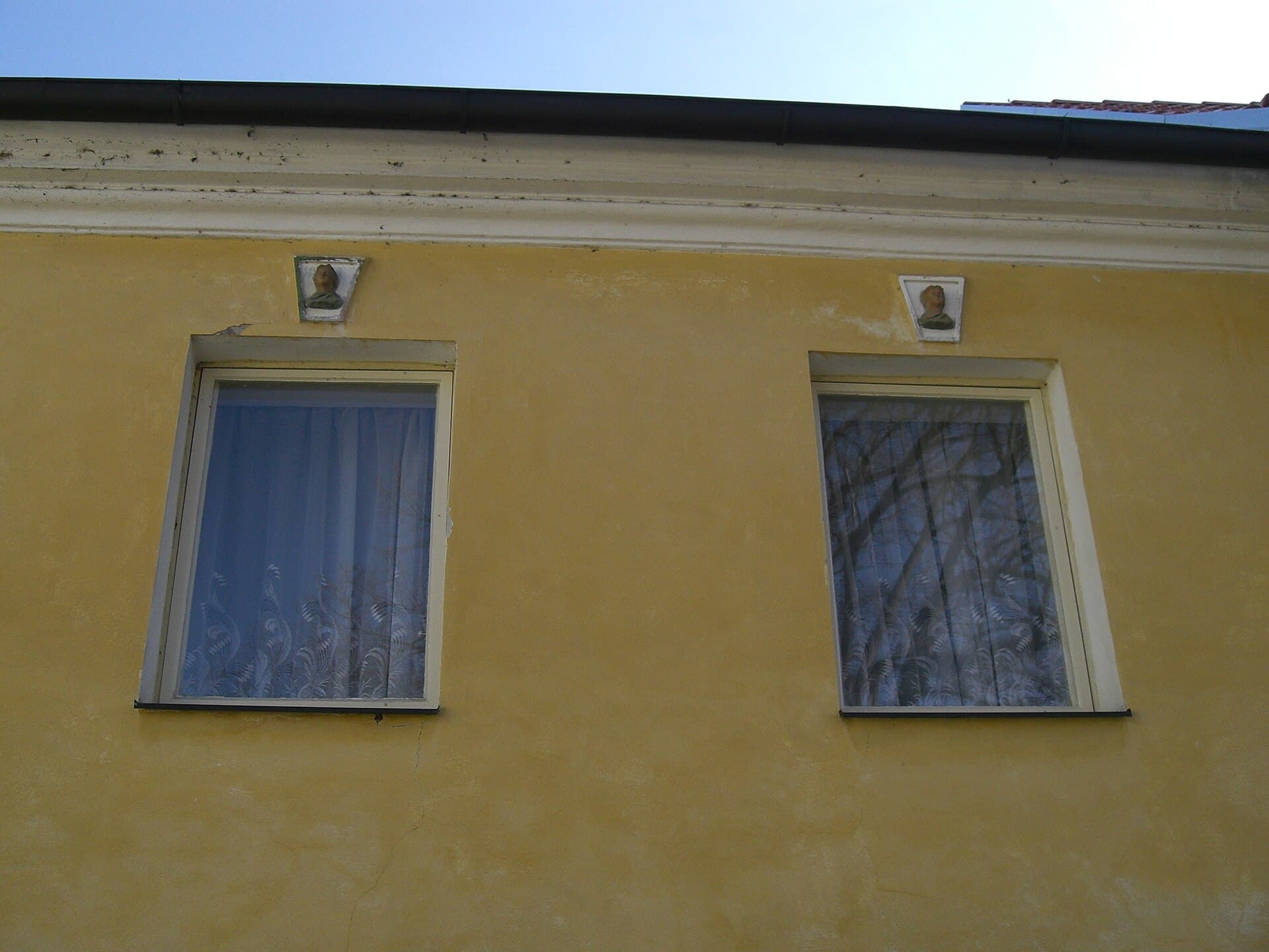 Dvě panenky nad okny domu nedaleko místa brány, připomínka úvodní sloky písně